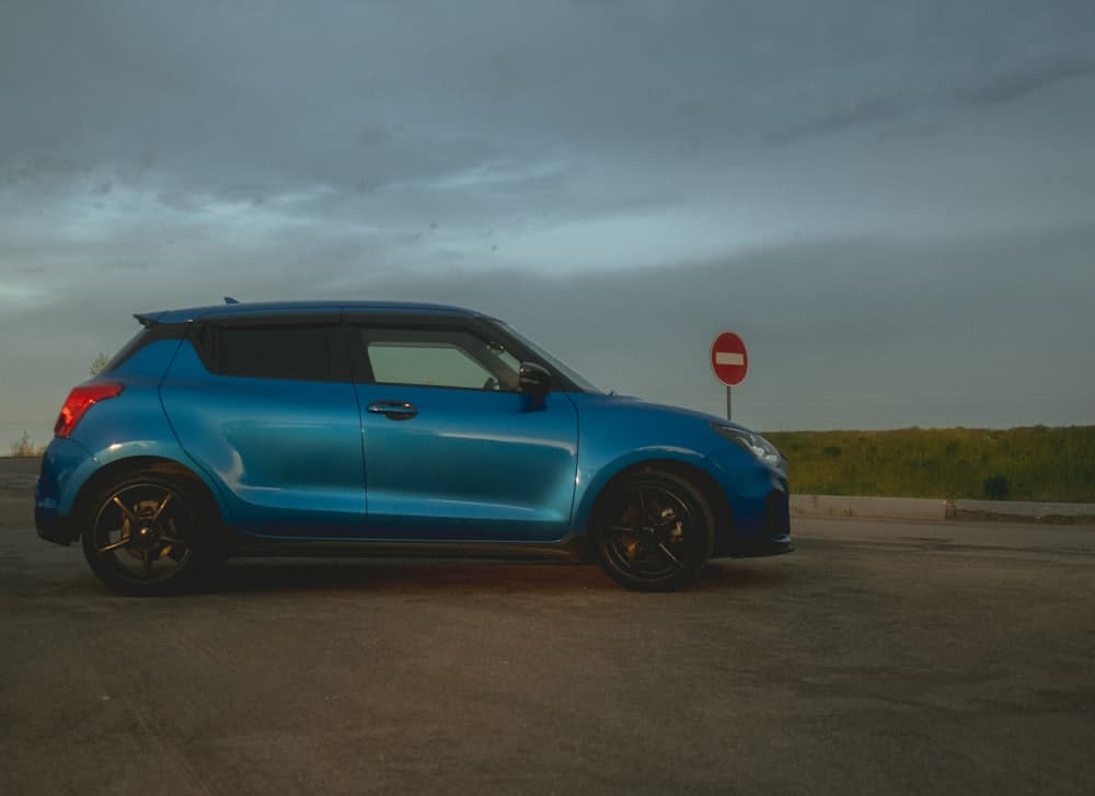 A compact blue hatchback parked on open ground under an overcast sky
