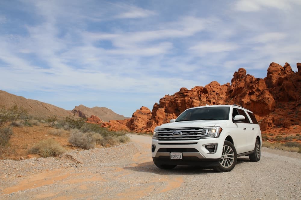 A white SUV parked on a desert track beside red rock formations